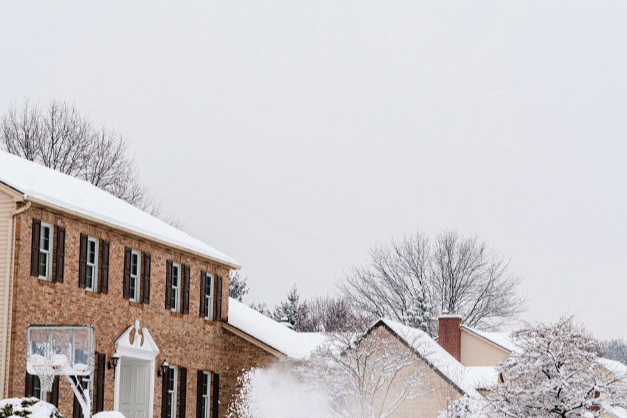 A person using a snow blower in front of a brick house
